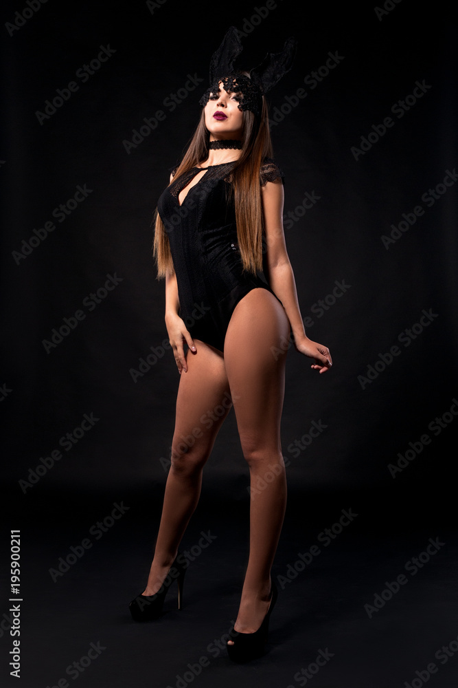 Sexy glamour girl in bodysuit, female wearing lingerie and shoes on black background with makeup and mask