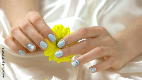 Chysanthemum in manicured hands, slow motion. Well-groomed hands with stylish manicure holding yellow flower on white silk background close up. Softness and purity concept. photo