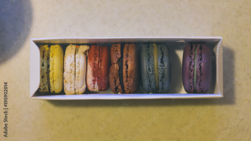 Macarons are on white stone table. Macarons are putted in a white paperboard box. Macarons are on white stone table. Macarons are putted in a white paperboard box.