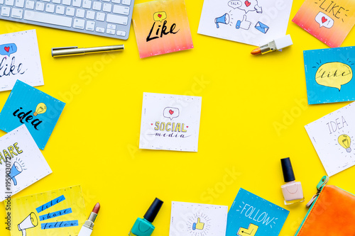 Beauty blogging concept. Work desk with keyboard, cosmetics and social media icons on yellow desk top view