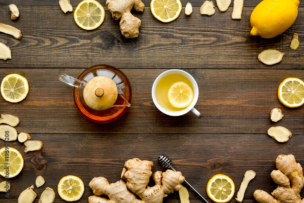 Tea for cure colds. Cup, teapot, ginger root and lemon on dark wooden background top view Tea for cure colds. Cup, teapot, ginger root and lemon on dark wooden background top view