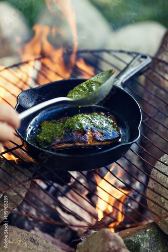 Salmon cooking over fire with pesto