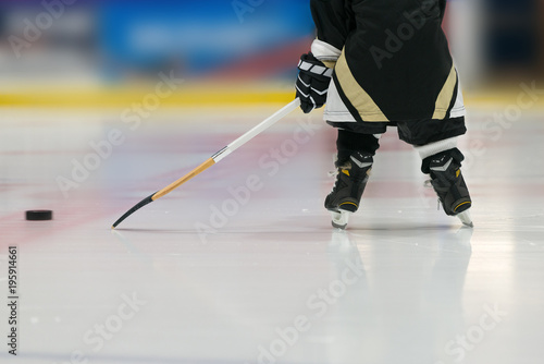 Toddler is playing hockey with stick and puck. Photo has been taken from back: skates and stick are shown. 