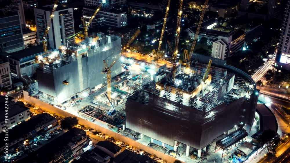 Time-lapse of construction site at night with light trails of traffic in the city, top view. Advanced building technology, busy metro downtown cityscape, or developing industrial country concept