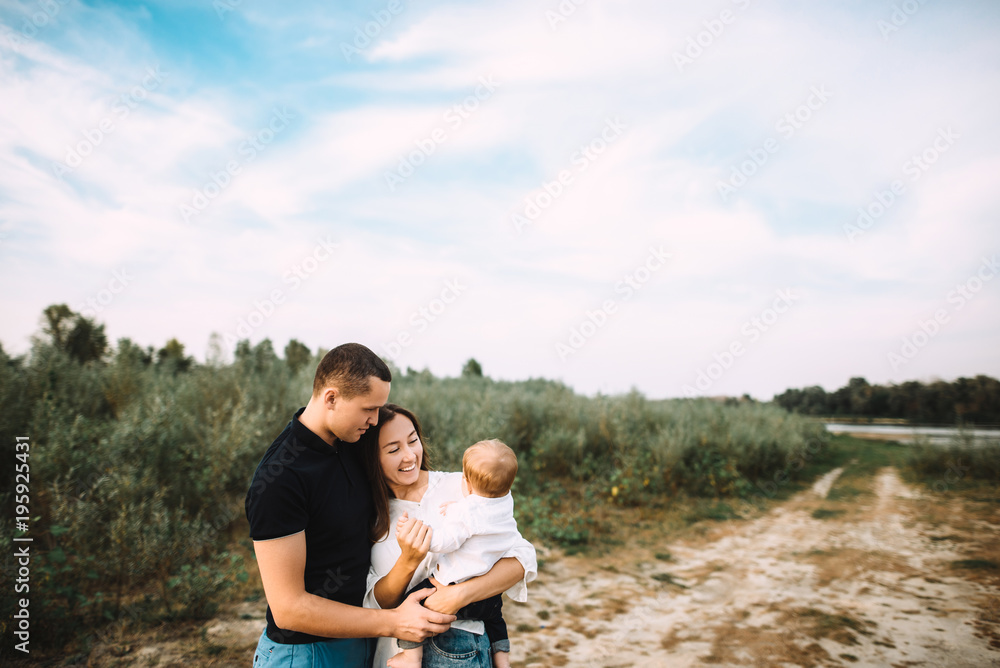 Happy young parents are walking in the countryside near the river with their little baby Happy young parents are walking in the countryside near the river with their little baby