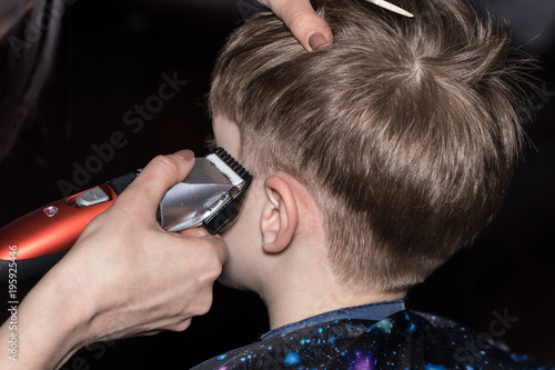 Side view of cute little boy getting haircut by hairdresser at the barbershop