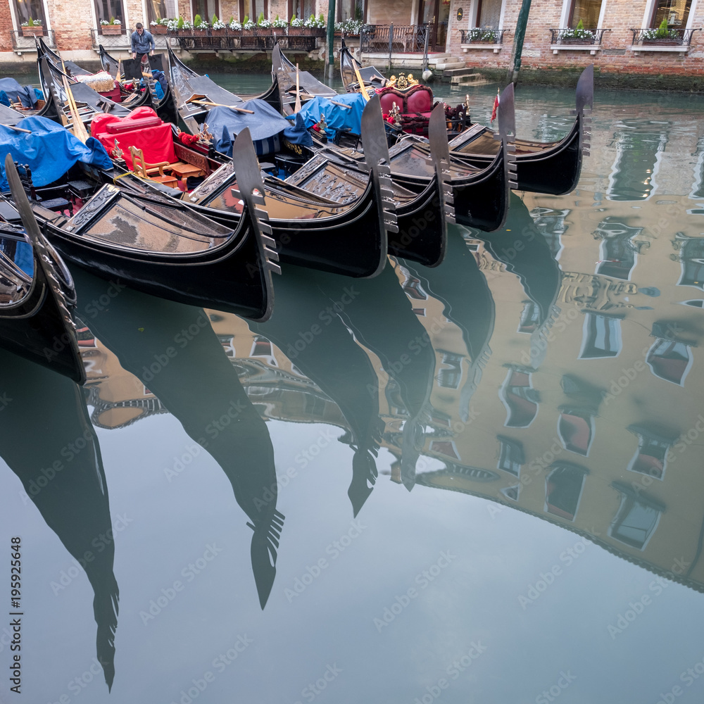 Close up of gondalas parked on a canal in Venice, Italy showing the decorative ferro / iron at the bow of the boats reflected in the water.