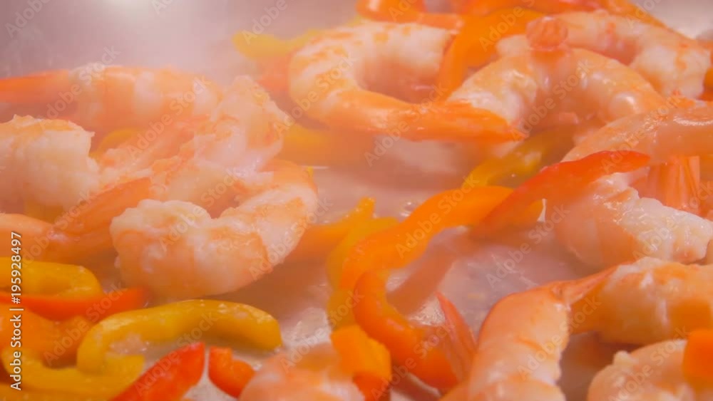 Close up peeled shrimps and paprika are falling into a skillet with oil Close up peeled shrimps and paprika are falling into a skillet with oil