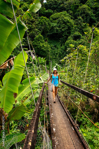 Young woman walking on suspension bridge over Wainibau stream, Lavena Coastal Walk, Taveuni Island, Fiji photo