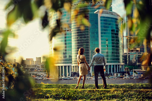 Foto Young couple in love watching the Moscow city skyscrapers at the sunset and hold