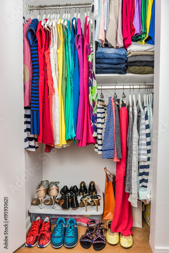 Fashion clothes in organized clothing closet shopping spending money. Many colors, colorful trendy outfits arranged in clean shelves and racks. Spring cleaning home living wardrobe.