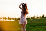 Girl in summer dress posing on sunset field background. Beautiful girl in meadow with sun rays young woman posing outdoors at nature with copy space
