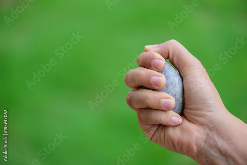 Close up Young woman hand holding stone on grass green background. Inspiration, Thinking and considering concept. © Siam