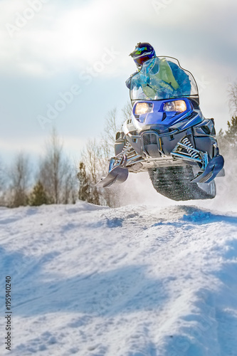 Sport blue snowmobile jump. Cloud of snow dust from under snowmobile tracks. Front view, vertical shot. photo