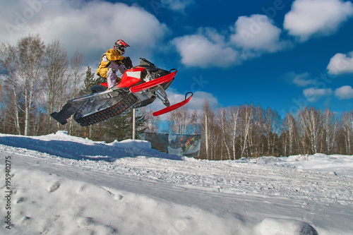 Sport red snowmobile jump. Sunny winter day with blue sky. Concept quick movement.