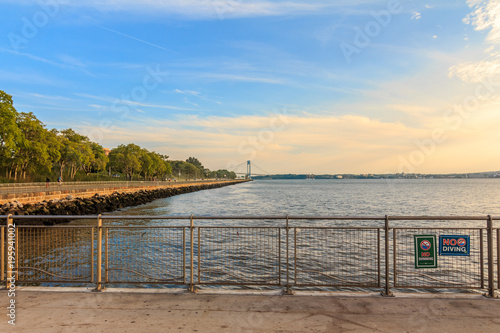 BROOKLYN, NY - 8/10/2017: Midday at Pier 69 in Bay Ridge with the view of the Belt Parkway and the Verrazano Bridge in the background under a blue, orange sky.