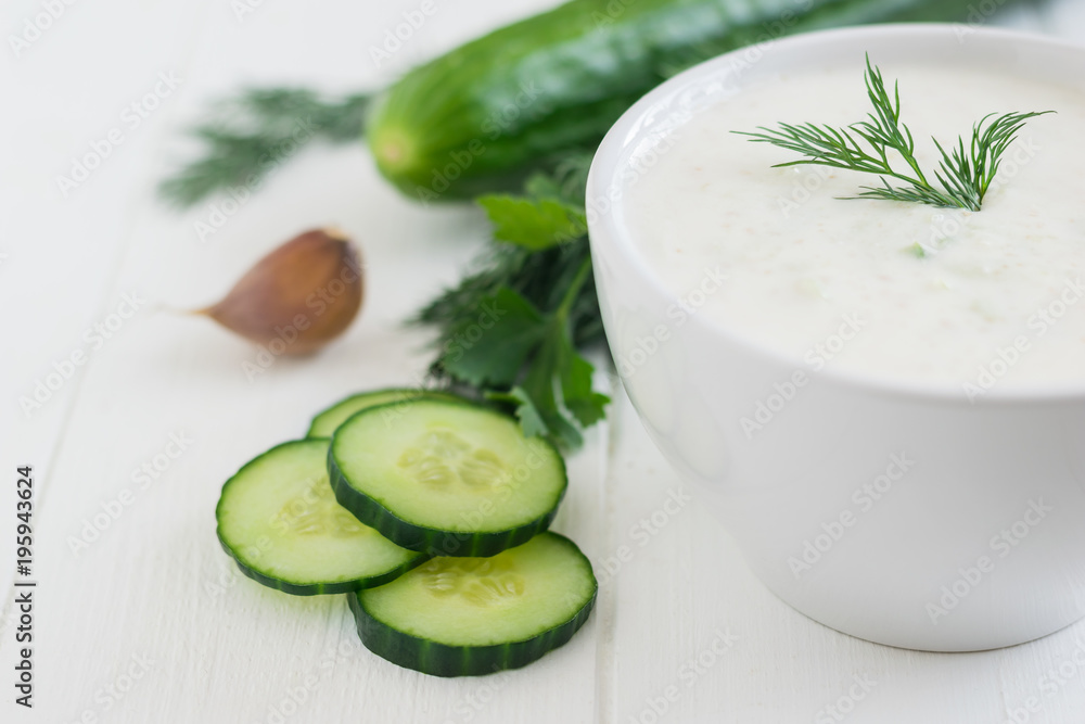 Freshly made tzatziki in a white bowl with cucumber and garlic on a white wooden table. Freshly made tzatziki in a white bowl with cucumber and garlic on a white wooden table.