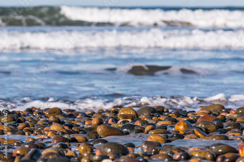 Stones covering South Carlsbad State Beach in San Diego, California with crashing waves in the background.