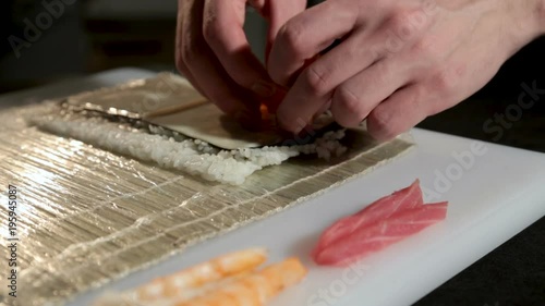 A man with his bare hands puts the salmon on the cheese. Japanese rolls. Close-up. white table. On the table ingredients for rolls. photo