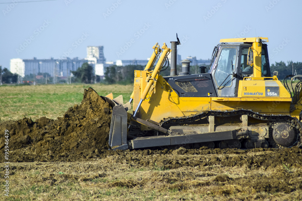 The yellow tractor with attached grederom makes ground leveling. The yellow tractor with attached grederom makes ground leveling.