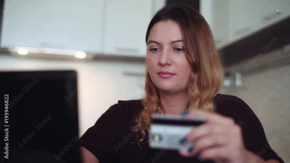 A beautiful young woman in dark clothes buys gifts with a credit card and a computer. Home style. A beautiful young woman in dark clothes buys gifts with a credit card and a computer. Home style.
