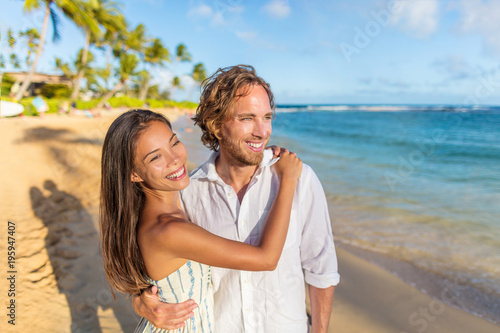 Happy couple in love on beach sunset vacation. Multiracial woman hugging husband people portrait on summer honeymoon travel holidays. Newlyweds portrait relaxing on beach at sunset. © Maridav