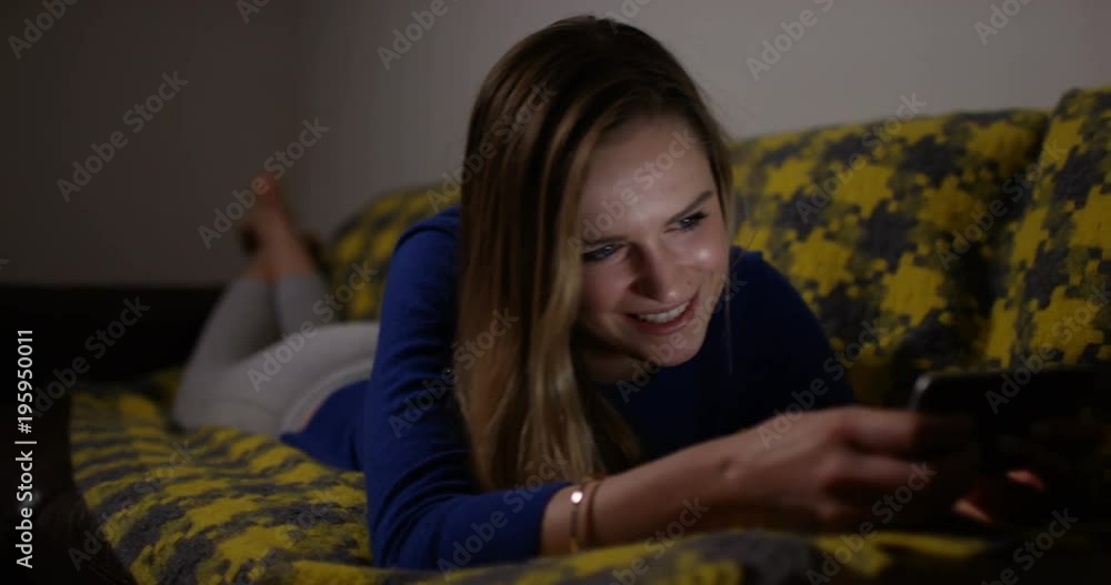 4K Happy girl relaxing at home at night, looking at her smartphone & laughing 4K Happy girl relaxing at home at night, looking at her smartphone & laughing