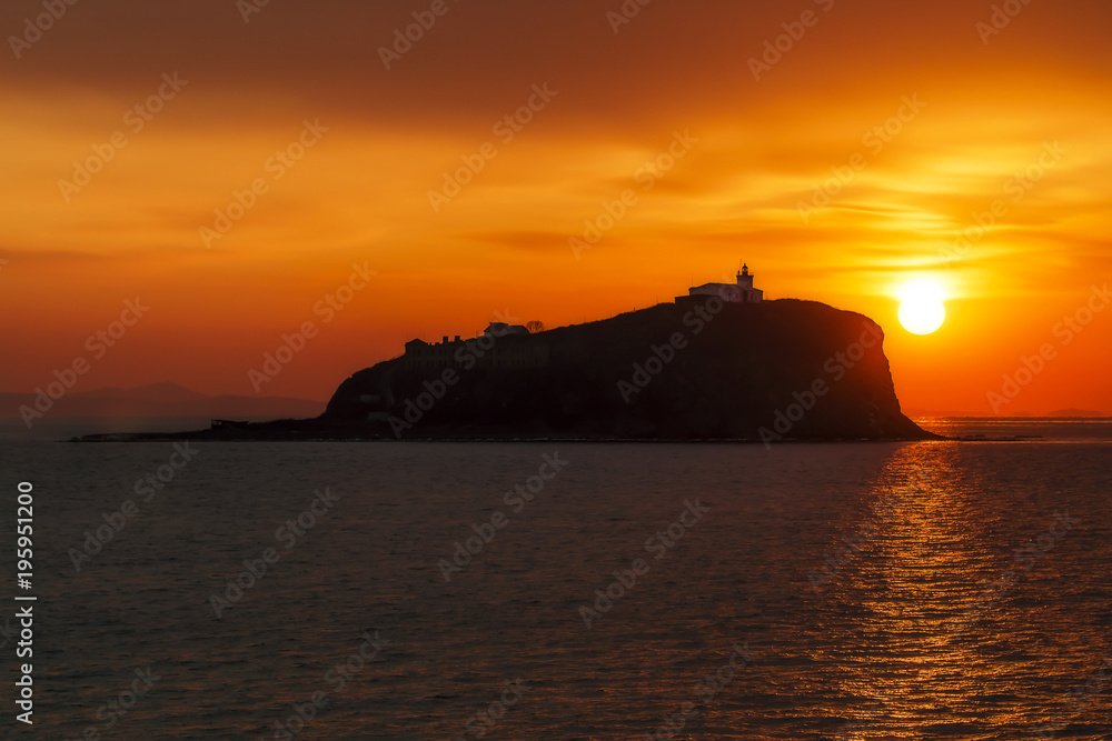 old lighthouse on the island against the sun