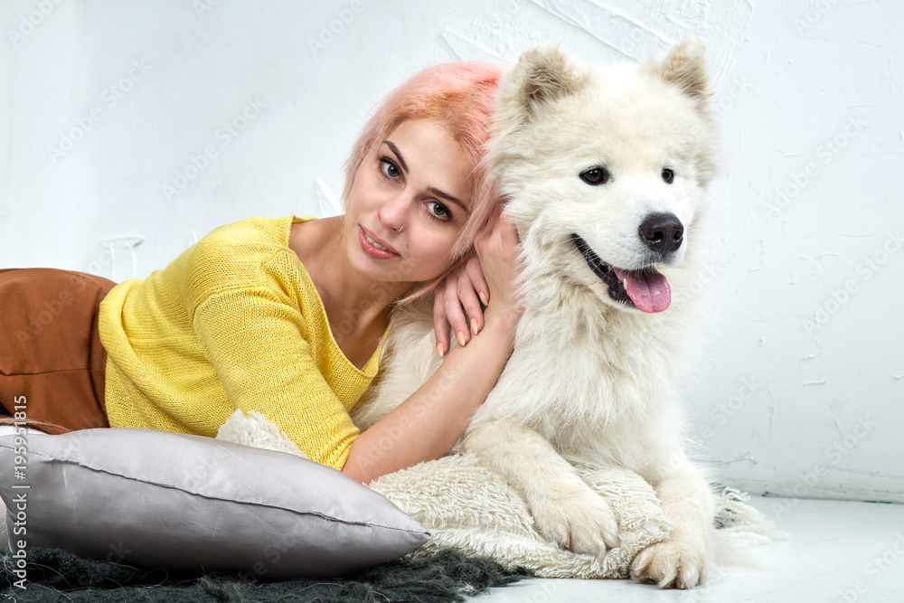 attractive young girl with her pet Samoyed posing lying on the white floor. Studio portrait with gentle warm tones. attractive young girl with her pet Samoyed posing lying on the white floor. Studio portrait with gentle warm tones.