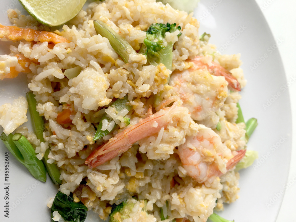 Fried rice with prawn herbs and vegetables served with lemon and cucumber in white plate on white background. Part of a series of nine Asian food dishes. Thai Food. Fried rice with prawn herbs and vegetables served with lemon and cucumber in white plate on white background. Part of a series of nine Asian food dishes. Thai Food.