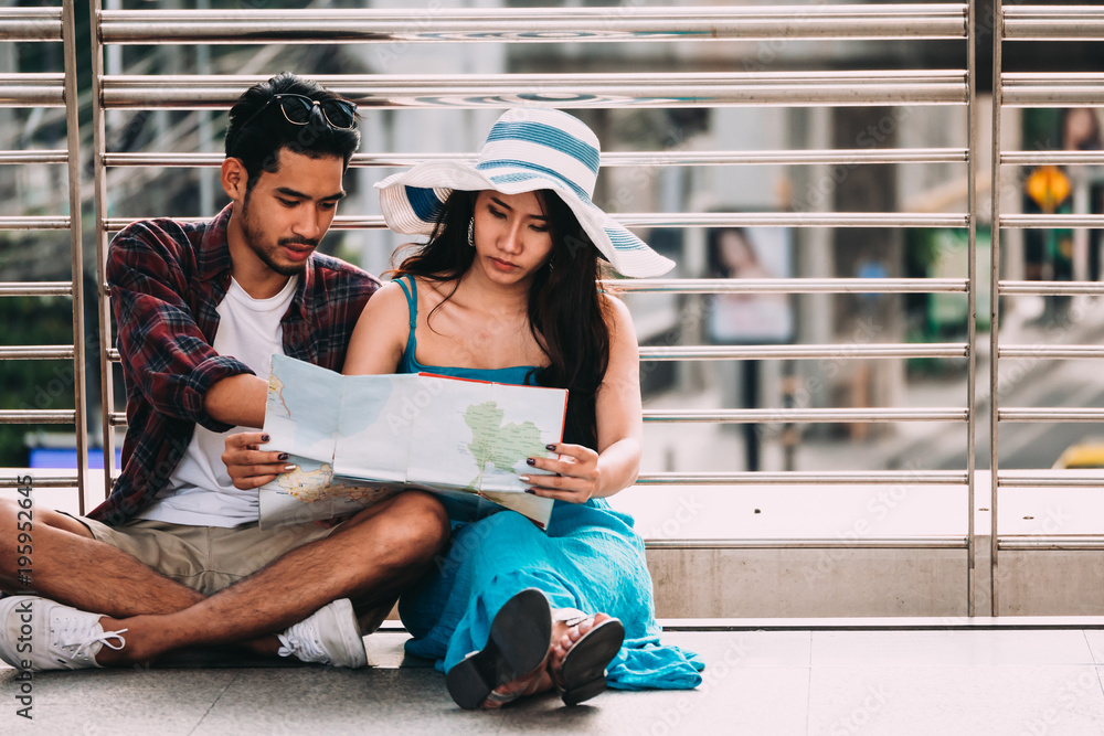 Couple Asian travelers are sitting on city street and looking at interesting places to travel from paper map. Vacation Concept. . Travel concept