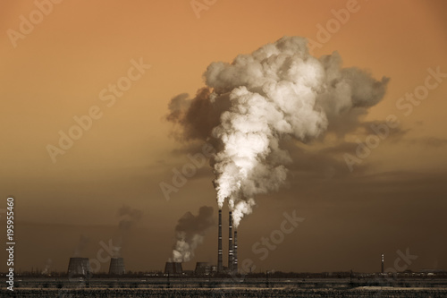 The thick smoke rises high from the industrial pipes. Pollution of the environment with waste products.