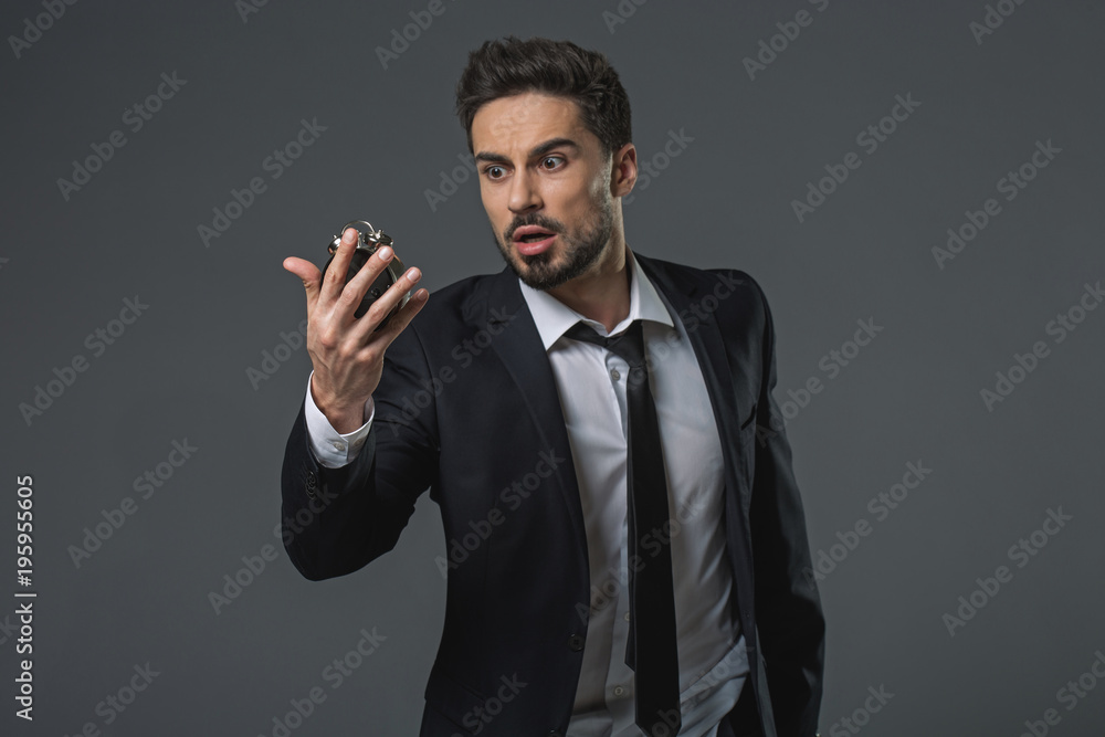 Waist up portrait of shocked businessman. He watching at snooze time with wide-eyed and open mouth in surprise. Isolated on grey background Waist up portrait of shocked businessman. He watching at snooze time with wide-eyed and open mouth in surprise. Isolated on grey background