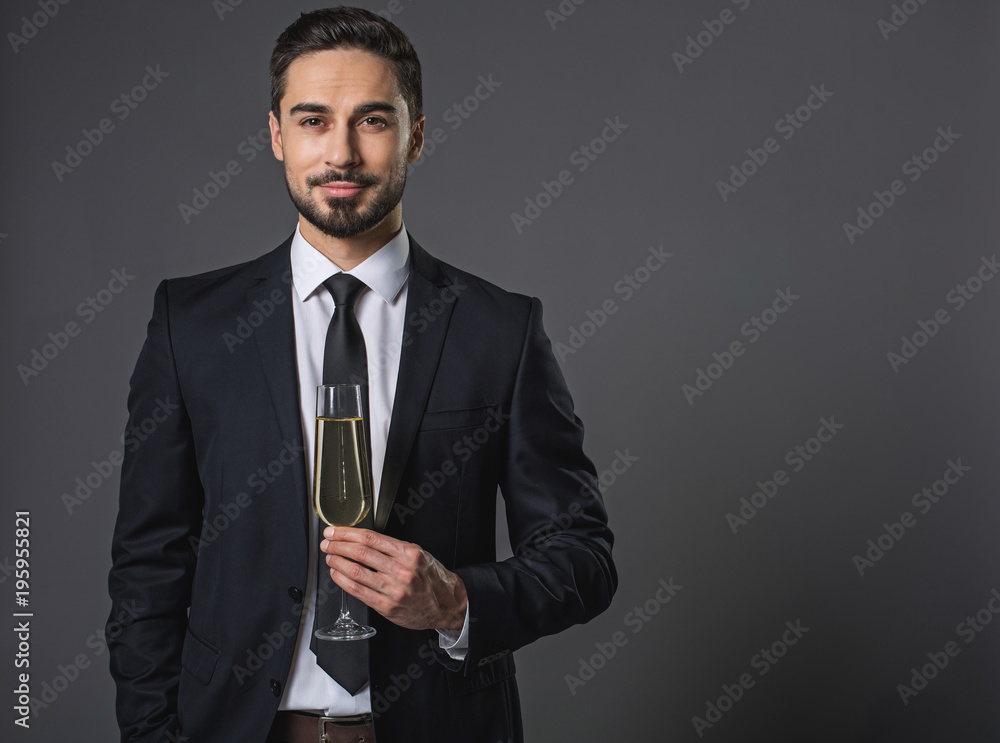 Waist up portrait of standing handsome and calm man in business suit with champagne. Isolated on gray background. Copy space in right side Waist up portrait of standing handsome and calm man in business suit with champagne. Isolated on gray background. Copy space in right side