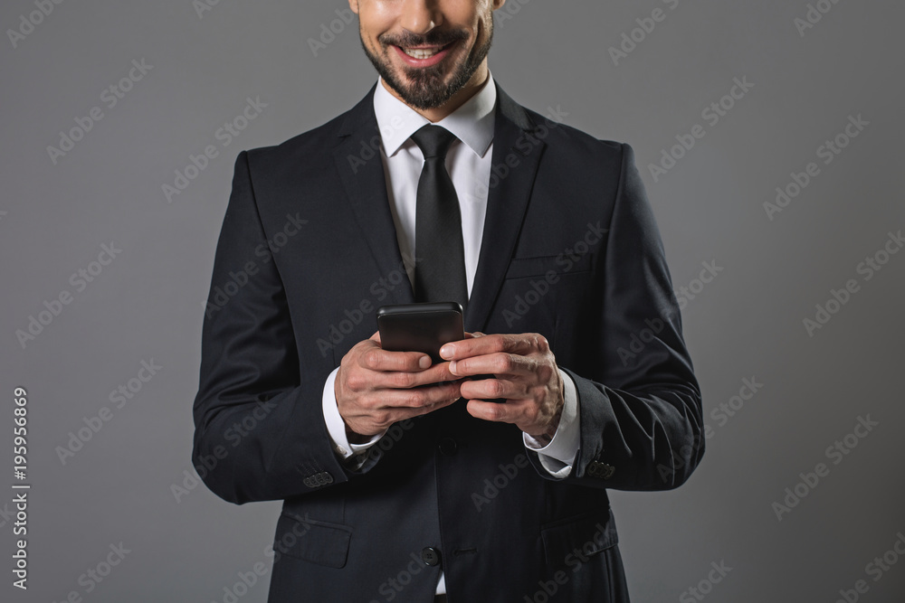 Young pleased man using modern cellphone. Businessman is standing. Isolated on gray background Young pleased man using modern cellphone. Businessman is standing. Isolated on gray background
