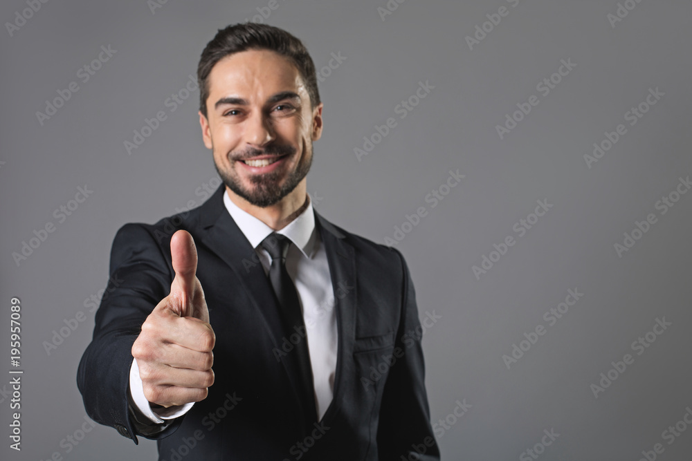 It is great. Waist up portrait of standing young smiling businessman showing ok sign. Isolated on grey background and focus on hand. Copy space in right side It is great. Waist up portrait of standing young smiling businessman showing ok sign. Isolated on grey background and focus on hand. Copy space in right side