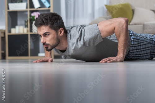 Stern handsome male pushing up on floor in living room. Low angle