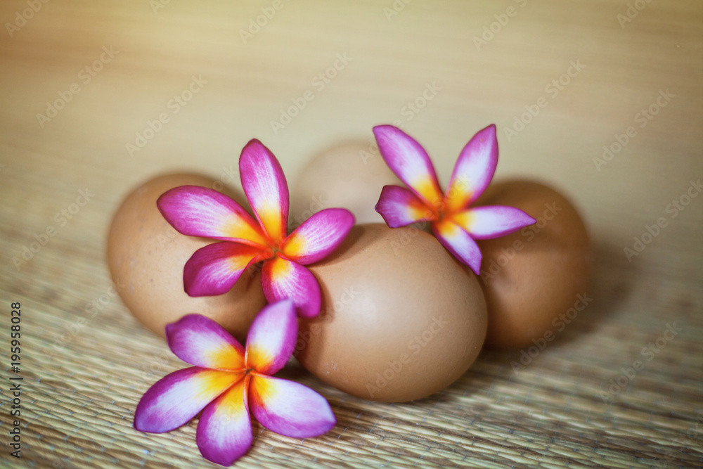 Four natural brown eggs with flowers are lieing on the straw rug Four natural brown eggs with flowers are lieing on the straw rug