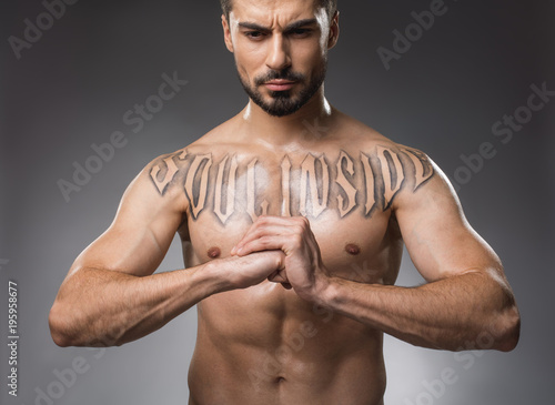 Force concept. Portrait of powerful naked male person with grave face holding fist against his palm. Isolated on background photo