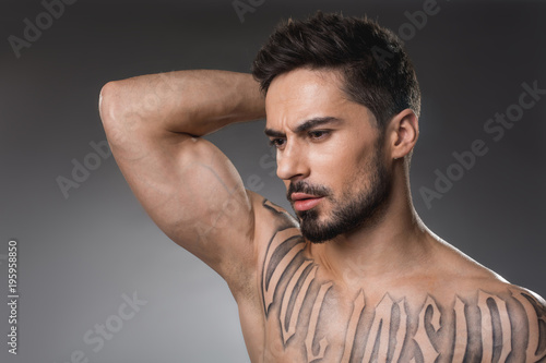 Beauty concept. Pensive man with strong muscularity holding hand on back of his hand. Isolated on background photo