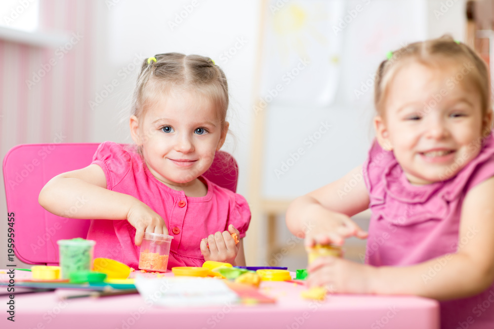 Fototapeta premium Two cute preschooler girls having fun together with colorful modeling clay at a daycare. Creative kids molding in nursery at home. Children playing with plasticine or dough.