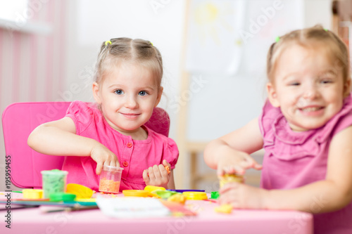 Two cute preschooler girls having fun together with colorful modeling clay at a daycare. Creative kids molding in nursery at home. Children playing with plasticine or dough.