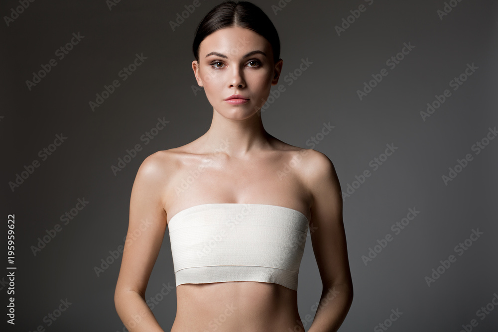 Waist up portrait of confident young slim woman standing with bandage wrapped over her breast. Isolated Waist up portrait of confident young slim woman standing with bandage wrapped over her breast. Isolated