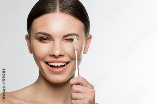 Portrait of excited young woman holding a toothbrush near her eye and laugh. Beauty and hygiene concept. Isolated and copy space