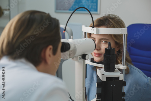 Happy woman inspecting eyes in ophthalmological center. Physician looking at special equipment. Optician clinic concept