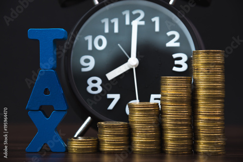 Time to pay TAX concept. TAX alphabet with stack of coin and vintage alarm clock in dark background, business and financial concept.