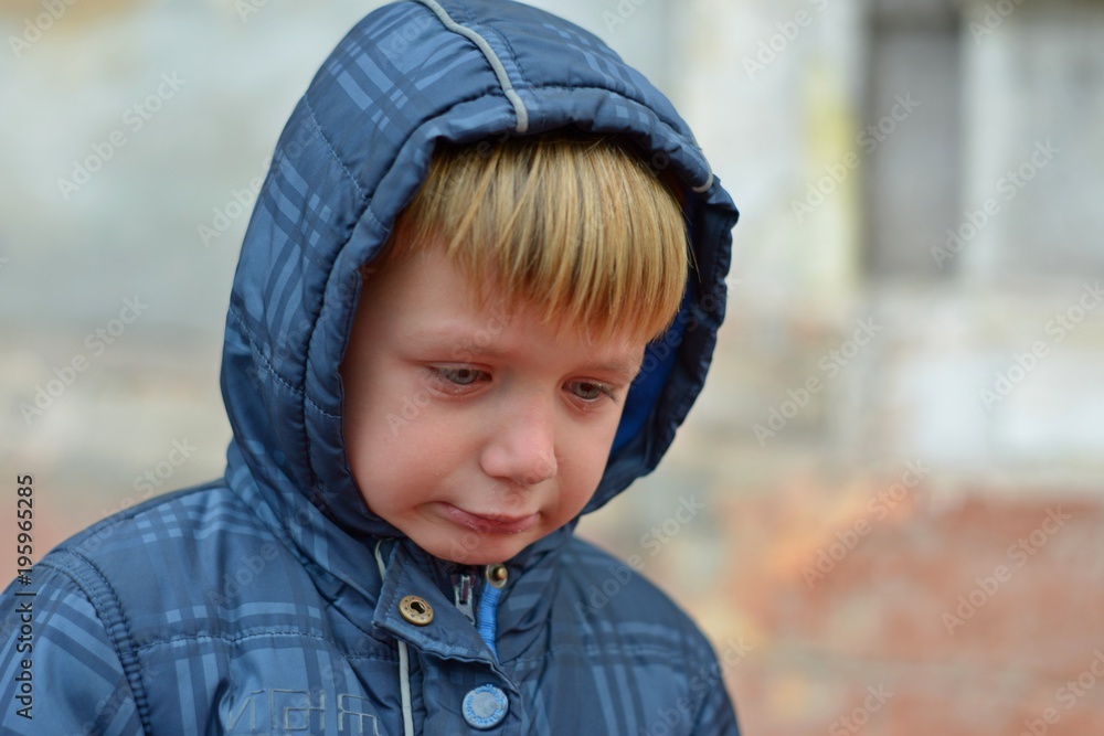 A boy in a blue jacket in a hood, crying with tears A boy in a blue jacket in a hood, crying with tears
