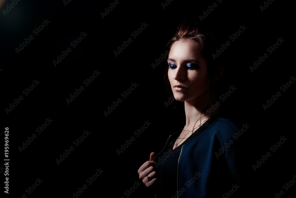 A woman in the fashion style with a professional make-up clings to the edge of her jacket and looks down on a black background with space for text A woman in the fashion style with a professional make-up clings to the edge of her jacket and looks down on a black background with space for text
