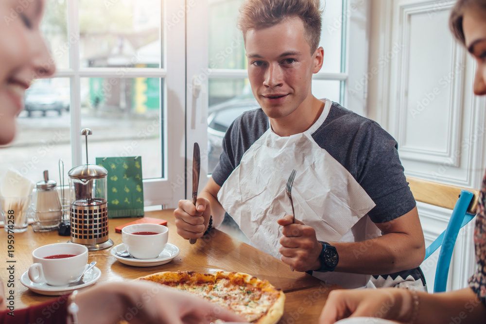 Stylish teenager wearing napkin holding knife and fork ready to eat pizza sitting against window at restaurant Stylish teenager wearing napkin holding knife and fork ready to eat pizza sitting against window at restaurant