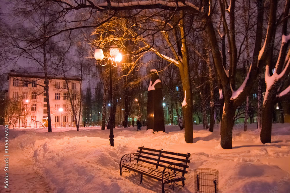 Naklejka premium Deep snow in the town park with benches, trees and street lights. Winter night photo park with snowdrifts 